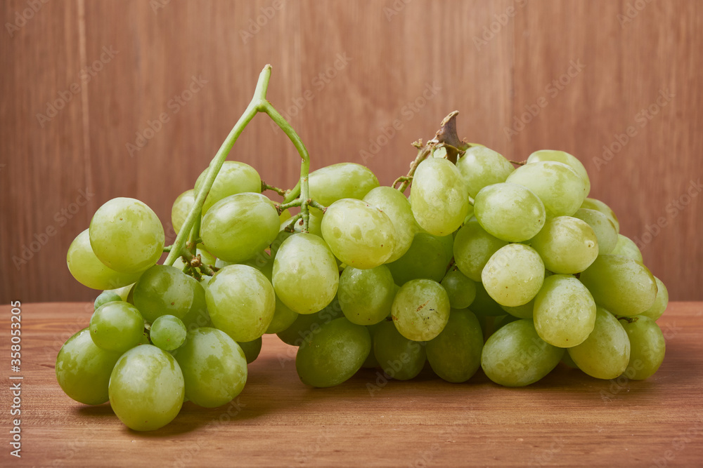 A bouquet of green grapes in a basket, autumn fruits, a symbol of abundance on a rustic background of a tree with a copy space, close-up. A bouquet of green grapes in a basket, autumn fruits, a symbol of abundance on a rustic background of a tree with a copy space, close-up.