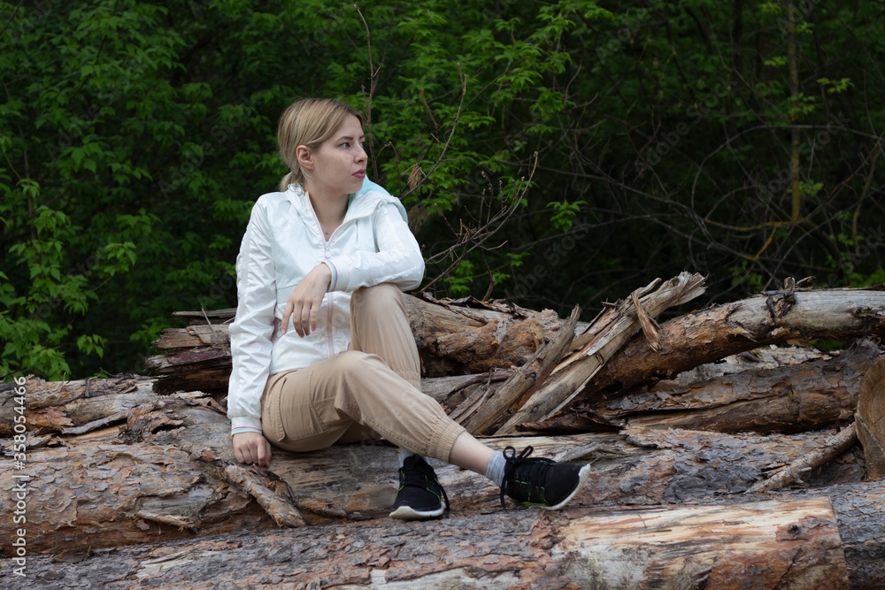 Fototapeta premium Outdoor close up portrait of young beautiful woman coat,sitting on a tree stump, Trees Chopped And Stacked In Forest