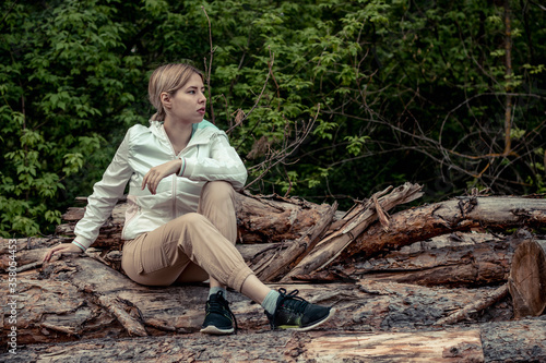 Outdoor close up portrait of young beautiful woman coat,sitting on a tree stump, Trees Chopped And Stacked In Forest