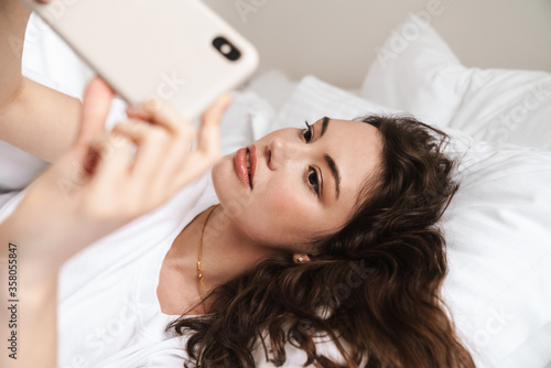 Photo of attractive woman taking selfie on cellphone while lying on bed