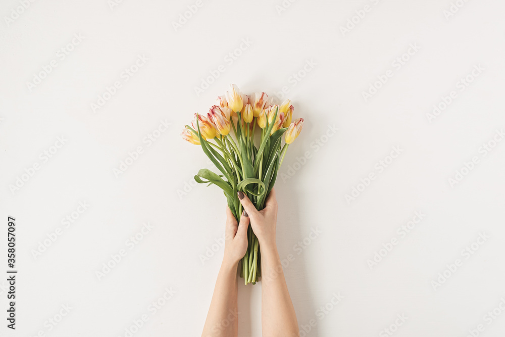Women's hands holding tulip flowers bouquet against white wall. Holiday celebration, wedding background