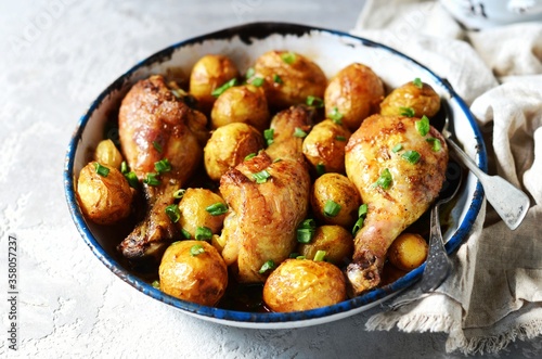 Baked chicken legs with young potatoes in a baking dish on a gray background