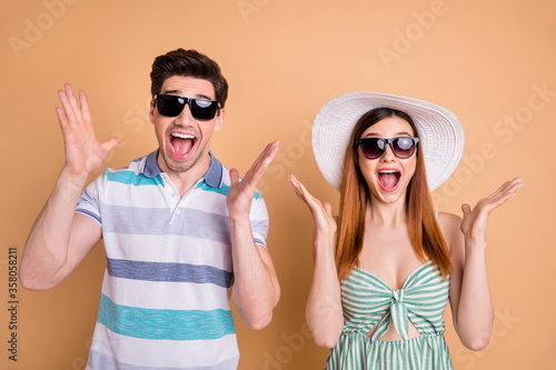 Photo of pretty lady handsome guy excited funky couple win free trip vacation journey addicted tourists wear casual summer clothes sun specs hat isolated pastel beige color background