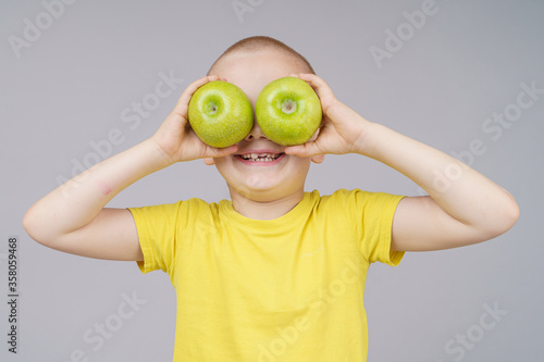 Smiling boy standing with fruit, holds apples instead of eyes. Isolated on gray © Quatrox Production