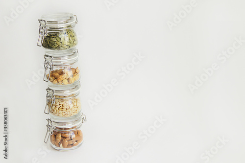 different types of nuts in glass jars stand one on one tower on a white background