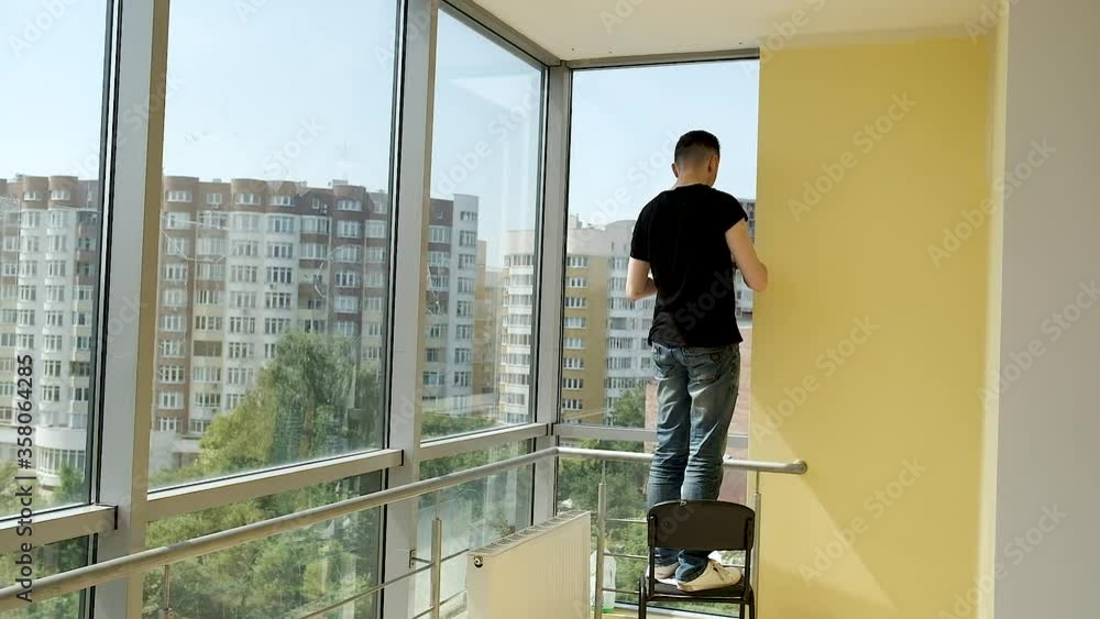 Young businessman makes repairs in his spacious office with panoramic windows. Painting the walls in white Young businessman makes repairs in his spacious office with panoramic windows. Painting the walls in white