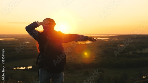 free girl tourist travels in nature alone. A young woman traveler with a backpack comes to edge of peak of sunrise  raises her hands in air and spins  enjoys victory  beautiful dawn and landscape.