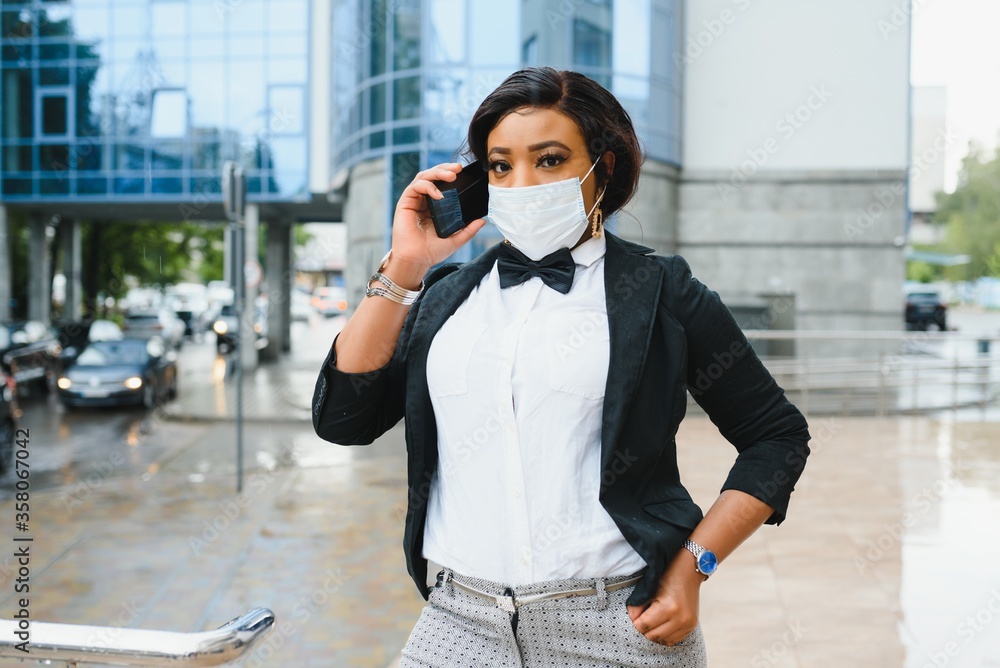 Fototapeta premium African American businesswoman wearing protective mask on her face in the city. The concept of visiting work during a pandemic