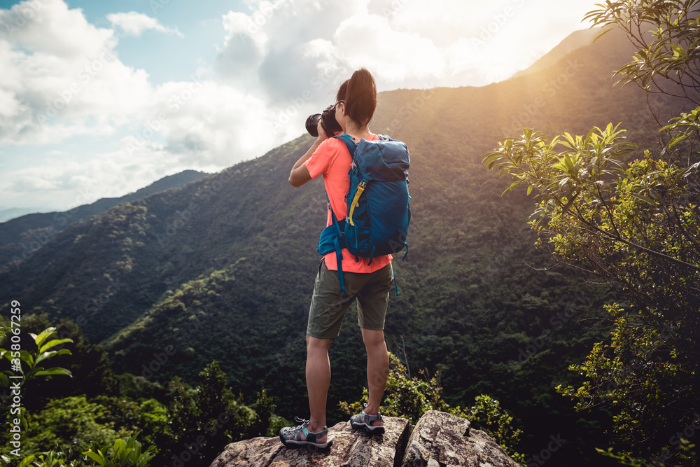 Woman photographer taking pictures on top of summer mountains