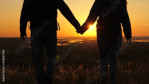 Travelers, man and a woman with backpack go to edge of mountain in rays of dawn, raise their hands in air and enjoy victory, beautiful sun and landscape. Free tourists travel. business teamwork