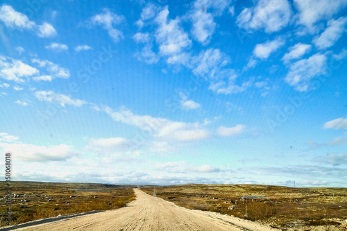 View from car windscreen with stripe relief to dirt country road  tundra and blue sky with white clouds in norht region at a sunny day