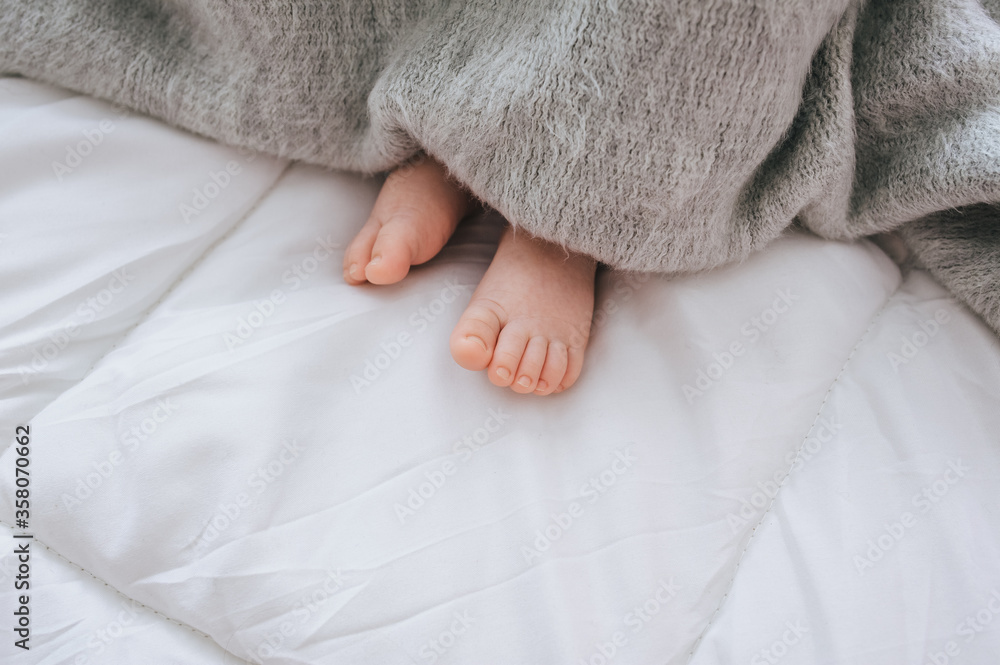A small child sleeps on a white bed, covered with a gray plaid close-up. The legs of the newborn. Photography, concept. A small child sleeps on a white bed, covered with a gray plaid close-up. The legs of the newborn. Photography, concept.