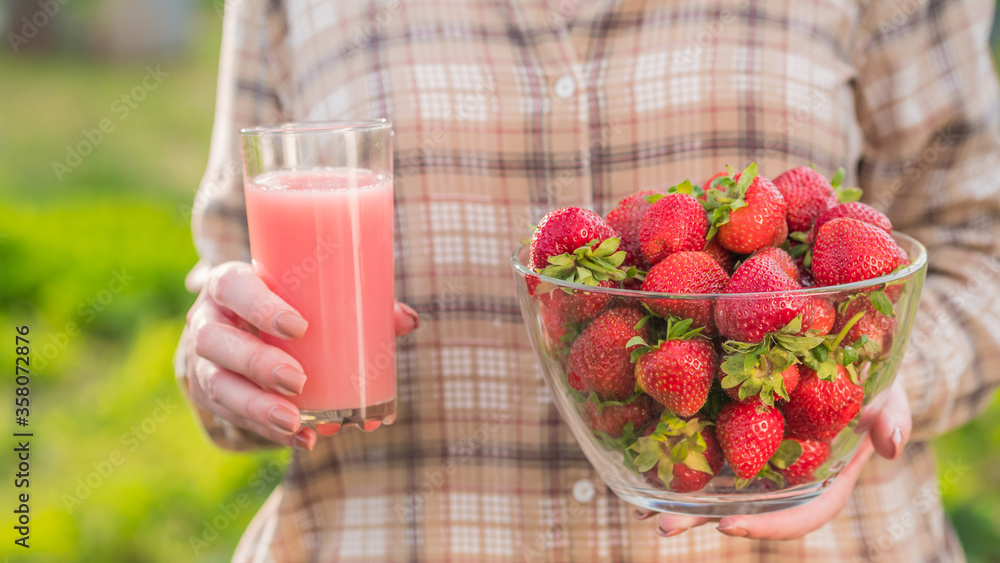 A slender woman holds a glass of juice and a bowl of strawberries. Delicious and healthy food