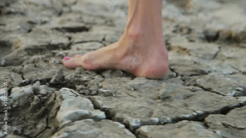 slim barefoot girl walks on dry cracked earth in slow motion