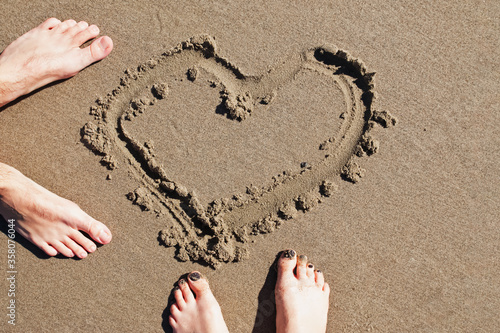 Feet of man and woman standing on the beacht with heart drawn on the sand photo