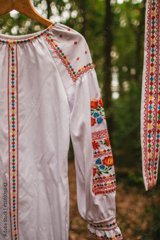 White Ukrainian national embroidered dress and belt on a hanger in the forest, close-up