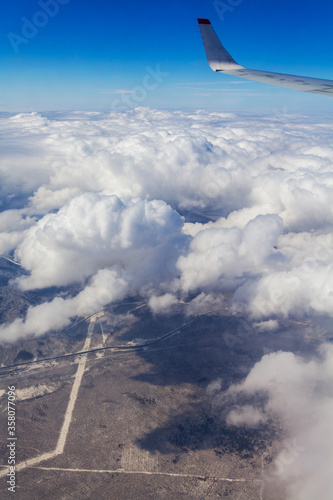 View of the airplane wing, clouds, blue sky, land under clouds.