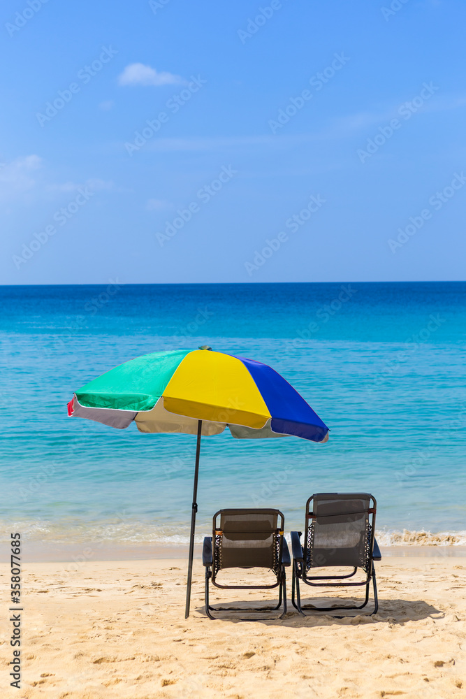 Relaxing by the beautiful beach, summer holiday, beach chair under colorful umbrella looking at blue sea ad clear blue sky