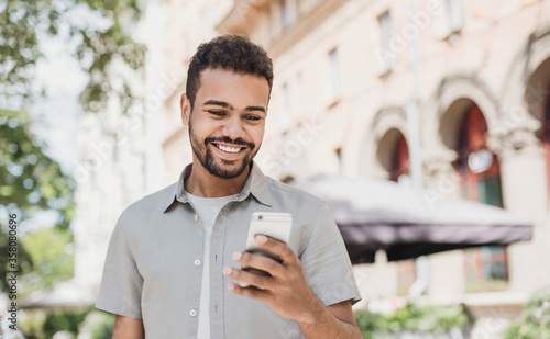 Young handsome student man using smartphone. Smiling joyful guy summer portrait. Cheerful men holding mobile phone