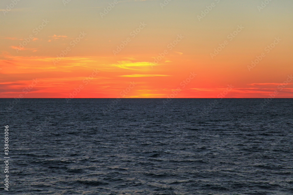 Fototapeta premium Morning on the high seas. Dark water and scarlet sky before sunrise. Seascape and background. Endless sea horizon, sadness and romance. Minutes of silence over the sea surface