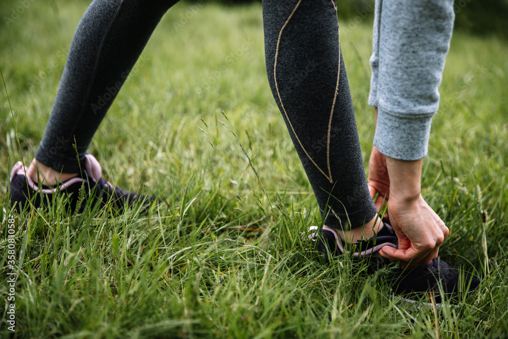 Young woman runner tying shoelaces in the grass