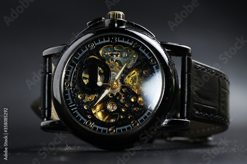 Black automatic self winding wristwatch with transparent sekeleton dial design on black leather background