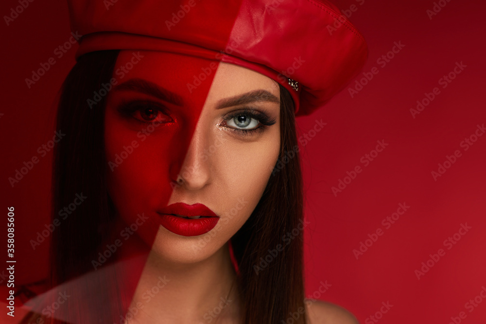 Beauty fashion portrait of brunette woman in red leather beret in studio on red background. girl with luxurious make-up looks through red colored glass. space for text Beauty fashion portrait of brunette woman in red leather beret in studio on red background. girl with luxurious make-up looks through red colored glass. space for text