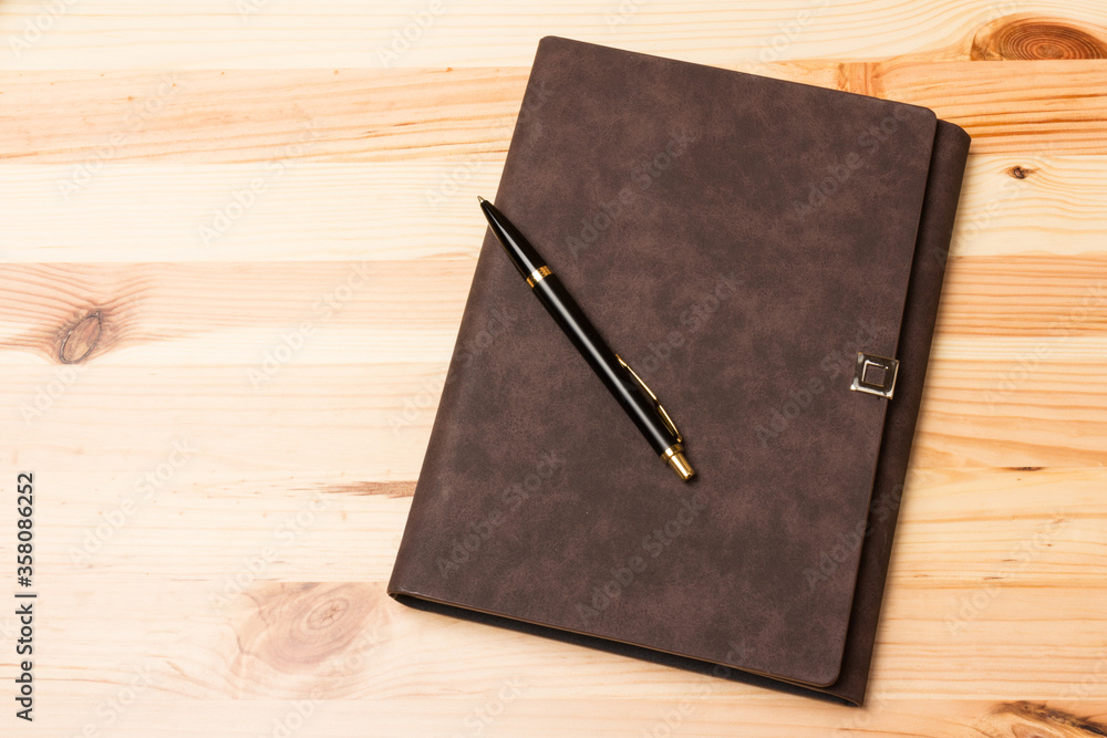 Leather-bound business notebook with a pen on wooden background. Leather-bound business notebook with a pen on wooden background.