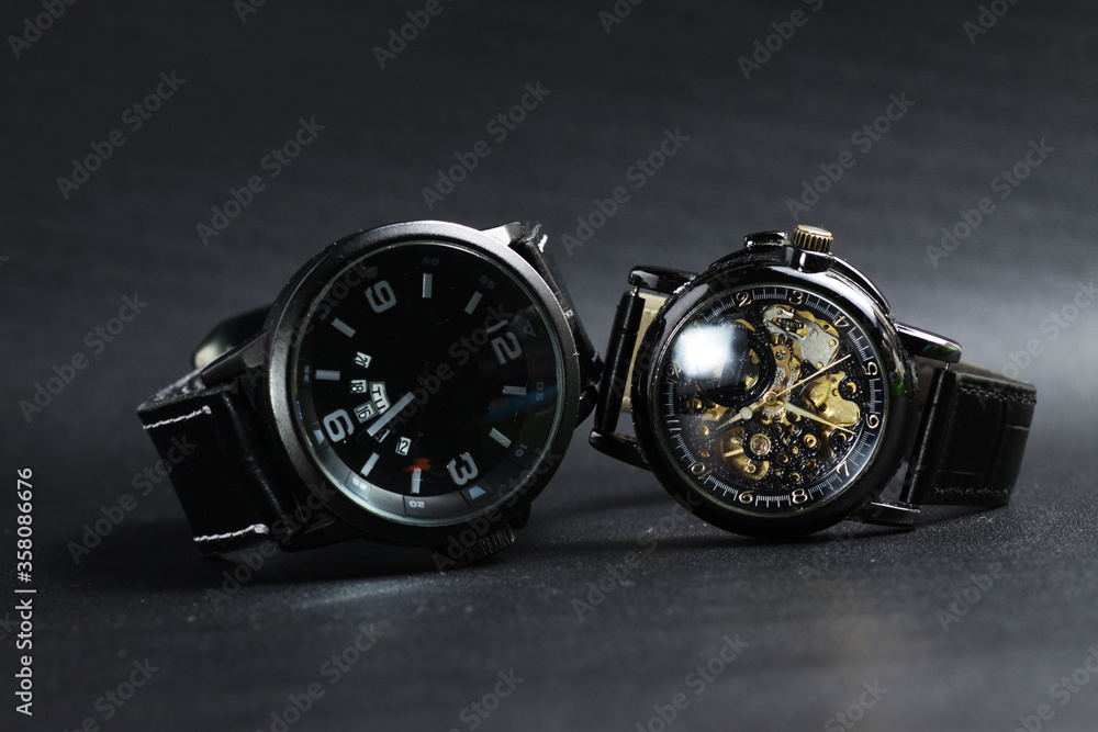 a black automatic self winding wristwatch with transparent sekeleton dial design and a black battery operated watch on black leather background a black automatic self winding wristwatch with transparent sekeleton dial design and a black battery operated watch on black leather background