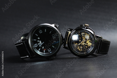a black automatic self winding wristwatch with transparent sekeleton dial design and a black battery operated watch on black leather background