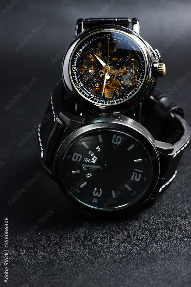 a black automatic self winding wristwatch with transparent sekeleton dial design and a black battery operated watch on black leather background a black automatic self winding wristwatch with transparent sekeleton dial design and a black battery operated watch on black leather background