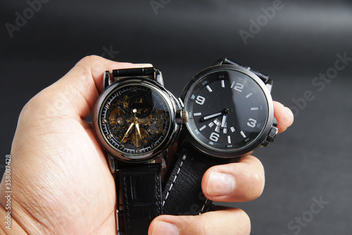 a black automatic self winding wristwatch with transparent sekeleton dial design and a black battery operated watch on black leather background