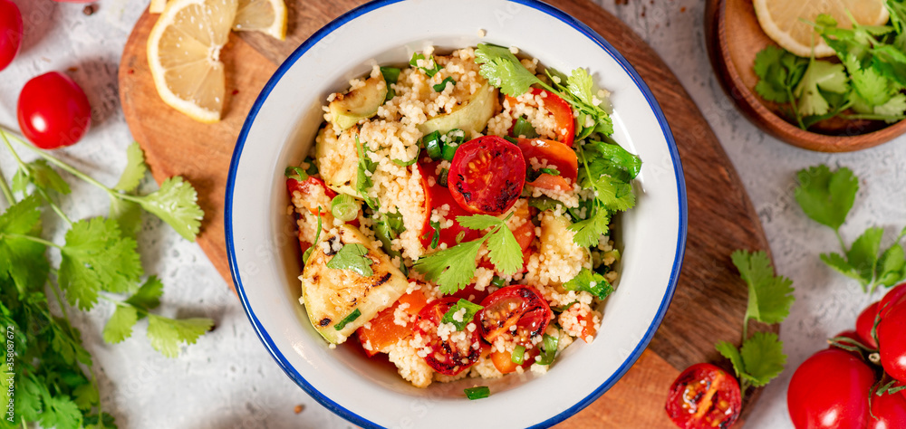 Salad of couscous and grilled vegetables in the bowl, cilantro, lemon and tomatoes on a gray concrete background top view. Vegan food. Arab or Middle Eastern cuisine. Salad of couscous and grilled vegetables in the bowl, cilantro, lemon and tomatoes on a gray concrete background top view. Vegan food. Arab or Middle Eastern cuisine.