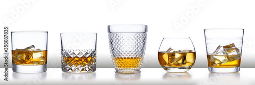 A white bar with a row of different style whisky glasses and ice, isolated on white