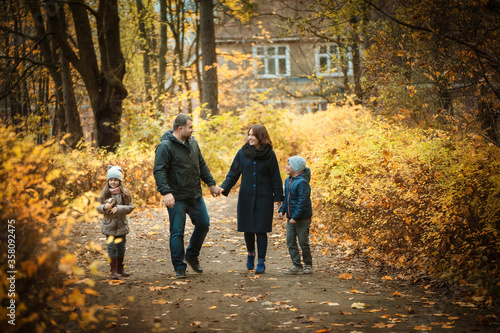 Sweet family walks along the path in the autumn park. Husband and wife hold hands, son and daughter walk together, they smile and talk. people are warmly dressed, they are in a good mood. Soft focus