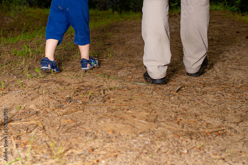 The legs of a father and a son against the background of nature. Dad and child walk forward in the woods. Family walk, Father's Day