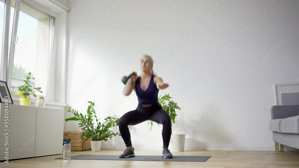 Athletic woman at home doing kettlebell exercises. Single Arm Kettlebell Squat Overhead Press Athletic woman at home doing kettlebell exercises. Single Arm Kettlebell Squat Overhead Press