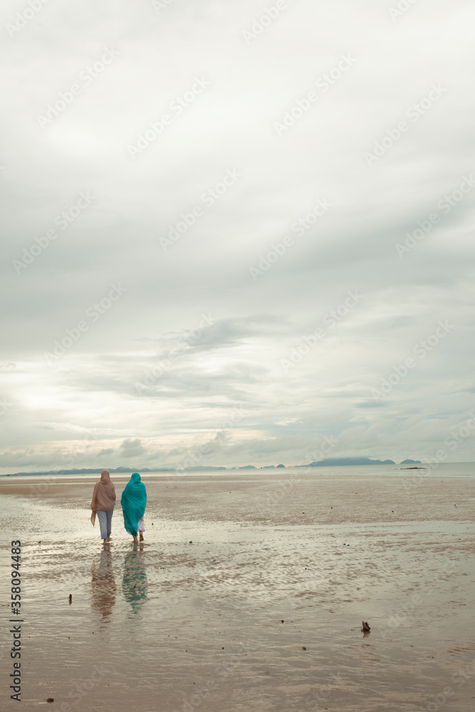 Lonely beach seascape with silhouette of two Muslim women walking at sunrise along the beach.