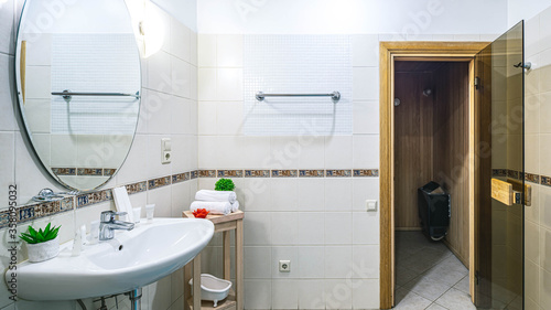 Light interior of modern spacious bathroom. Sink and mirror. Opened door to the wooden sauna.