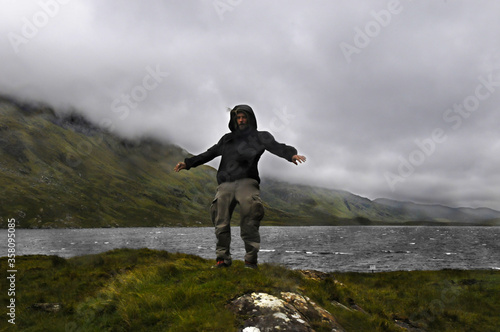 Homme se tenant difficilement debout au bord d'un lac en Irlande, le vent tempétueux et la pluie le poussant dans le dos. 