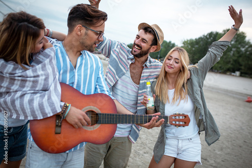 Group of friends hangout at the city beach.One guy plays guitar and singing while his friends dancing around him.	
