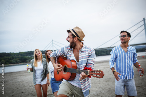 Group of friends hangout at the city beach.One guy plays guitar and singing while his friends dancing around him. 