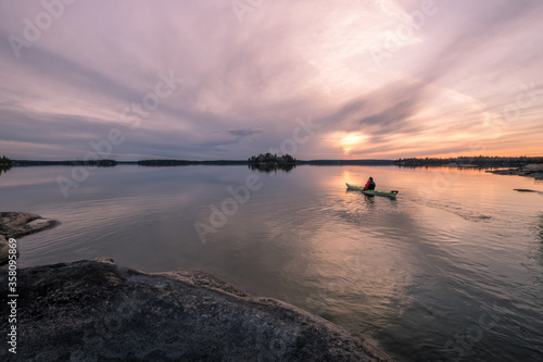 A lone kayaker paddles at sunset among the islands on a calm lake in Northwest Ontario, Canada.
