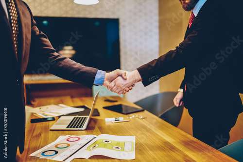 Cropped image of men in suits shaking hands making deal of sponsorship in business corporation, male entrepreneurs agree in partnership cooperation and contract during formal meeting in office photo