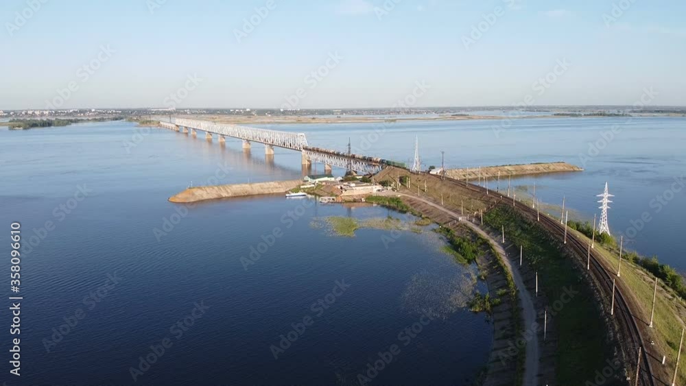 Aerial flying with locomotive pulls into a bridge over a river at sunset Aerial flying with locomotive pulls into a bridge over a river at sunset