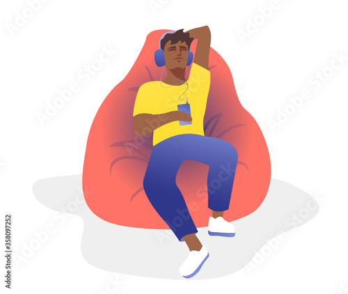 A handsome guy is resting in a bean bag chair with headphones. Relaxation concept to your favorite music.