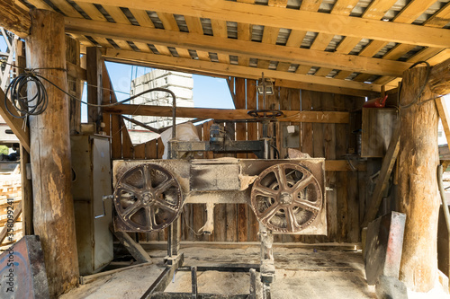 Sawmill under a canopy in the summer in the open air close-up of equipment for sawing and processing of wooden trunks with a large blade under torque.