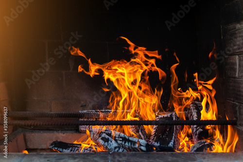A flaming bright yellow-red fire in a brick masonry on charred birch firewood for cooking barbecue or heating a country house.