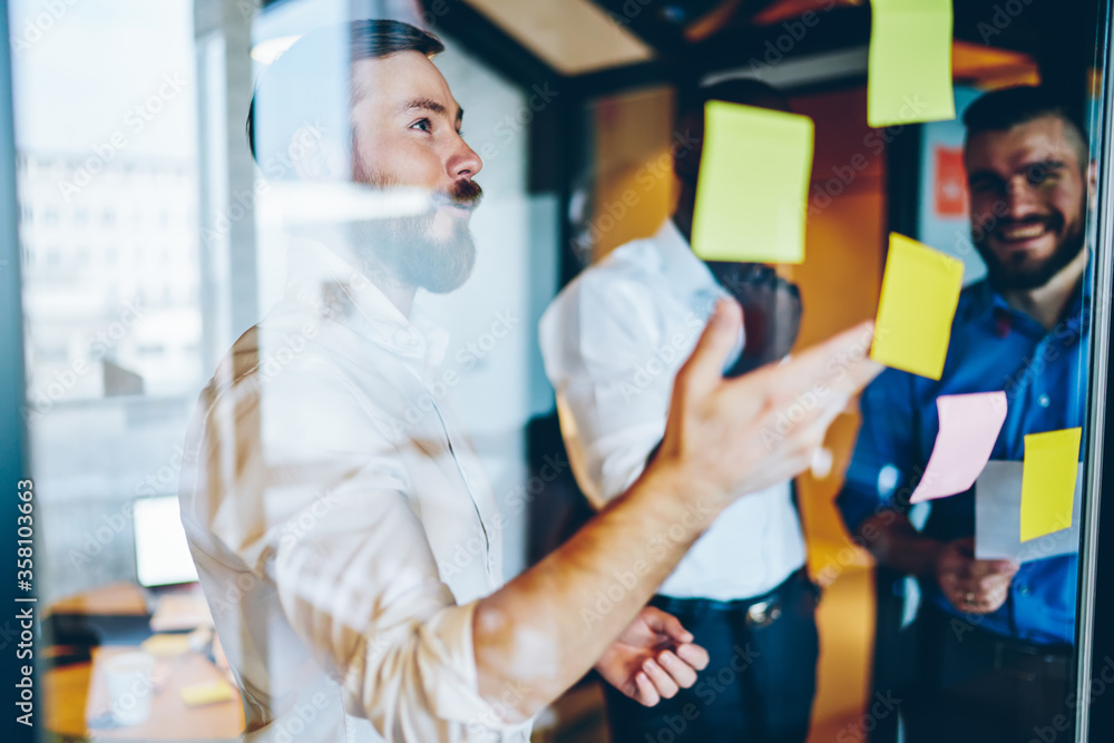 Obraz premium Cheerful multiracial colleagues discussing information on stickers on window