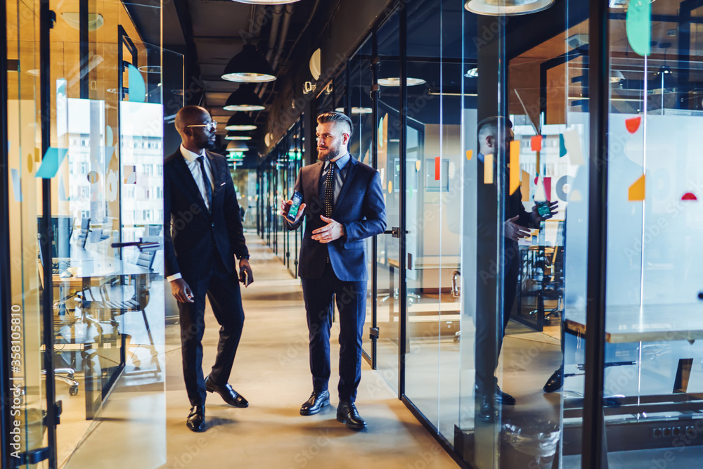 Pensive diverse executive men sharing ideas in light office corridor